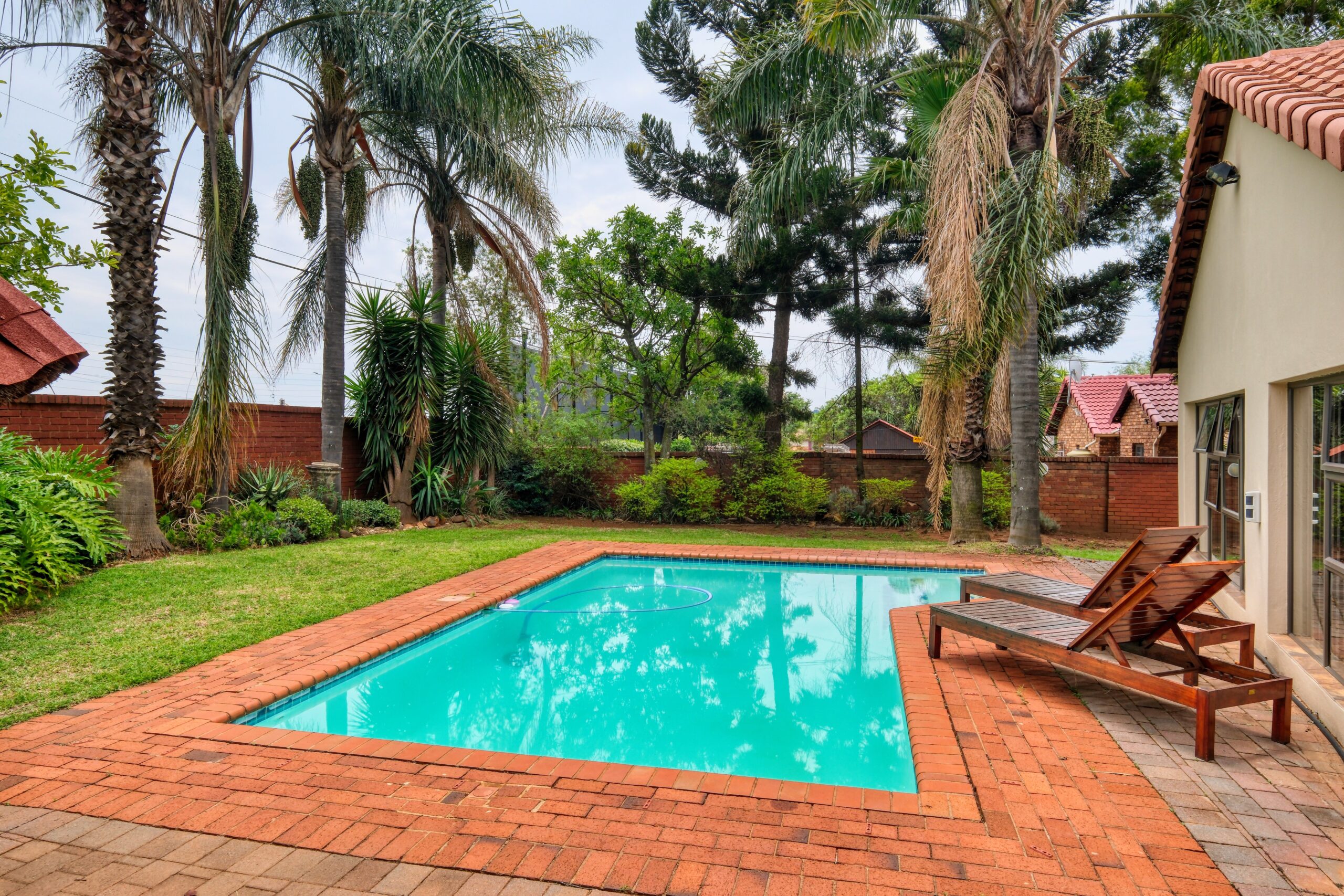 Discover relaxation in a backyard oasis featuring a pool, palm trees, and sunbeds in Pretoria, South Africa.